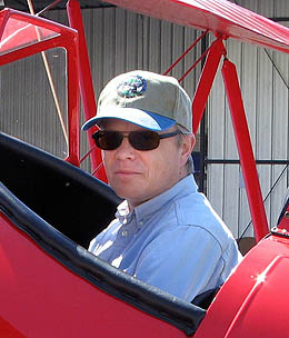 Closeup of a man sitting in the cockpit of a red biplane.